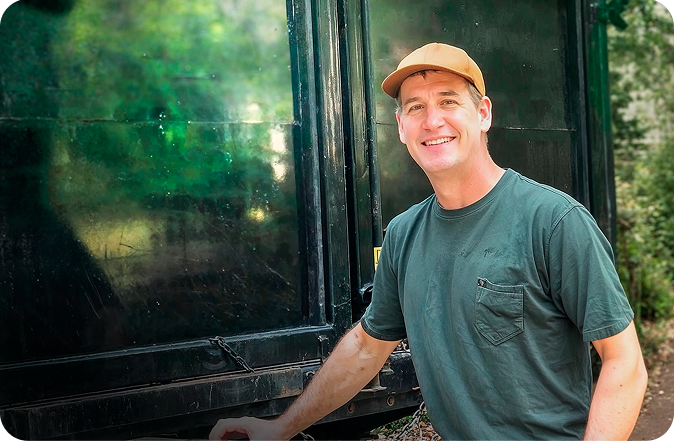 Smiling junk removal professional standing next to a large black service truck on a residential property.