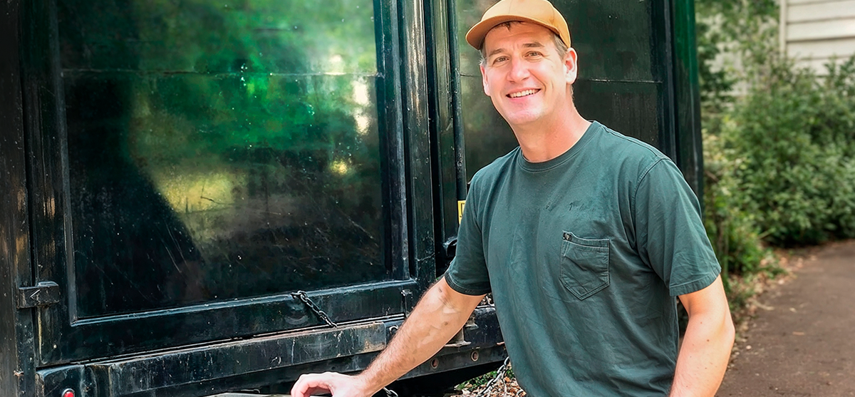 Smiling junk removal professional standing next to a large black service truck on a residential property.