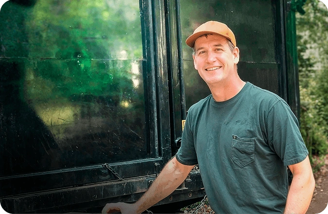Smiling junk removal professional standing next to a large black service truck on a residential property.