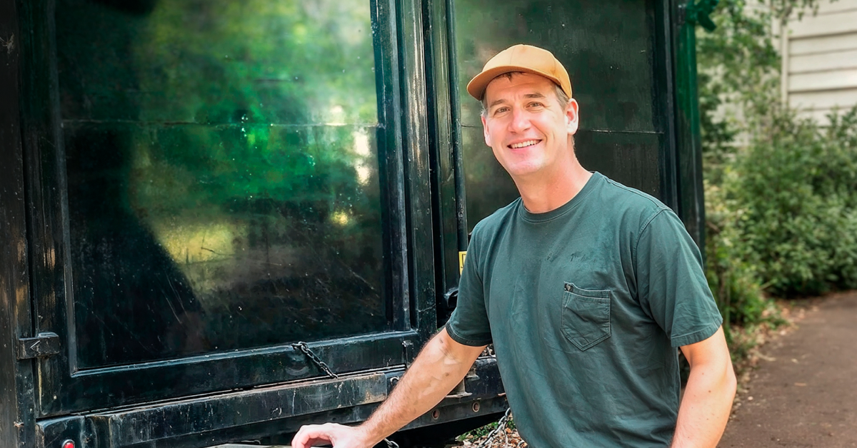 Smiling junk removal professional standing next to a large black service truck on a residential property.