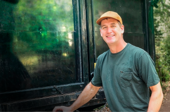 Smiling junk removal professional standing next to a large black service truck on a residential property.