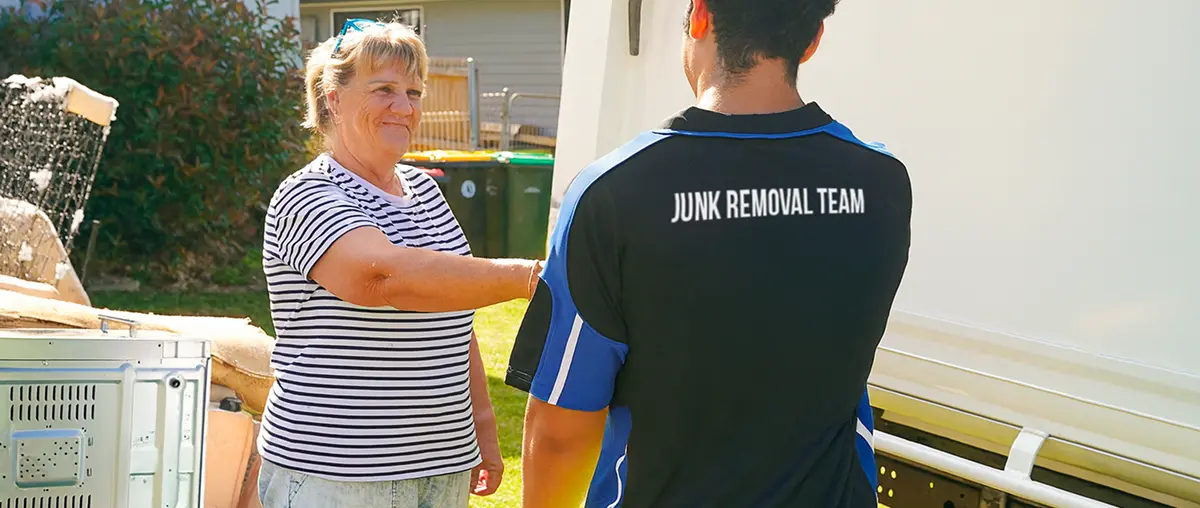 Smiling junk removal professional standing next to a large black service truck on a residential property.