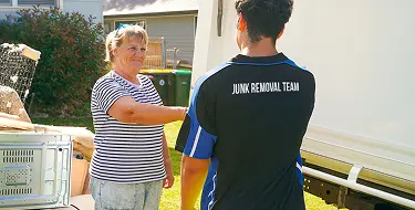 Smiling junk removal professional standing next to a large black service truck on a residential property.