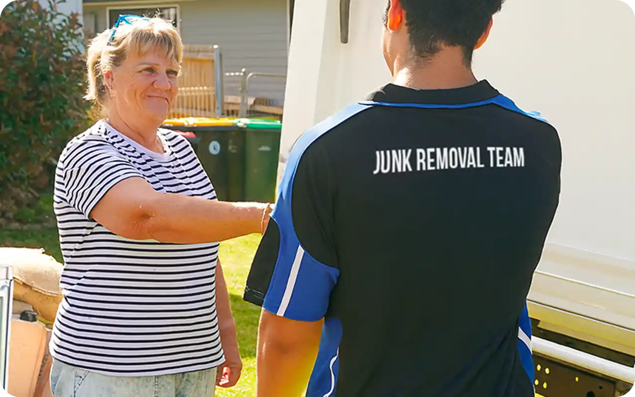 A smiling woman shaking hands with a member of a 'Junk Removal Team' outdoors near a residential driveway.
